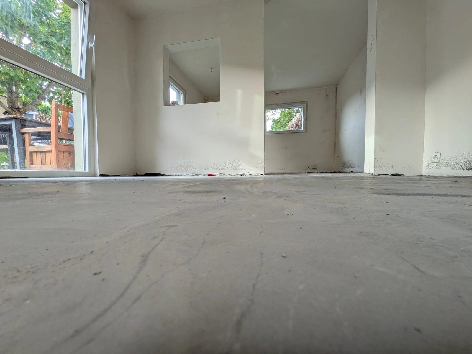 Blick knapp über dem frisch ausgeglichenen Boden durch den Anbau. Grau, glatt und endlich eben, links das große Fenster zum Garten.