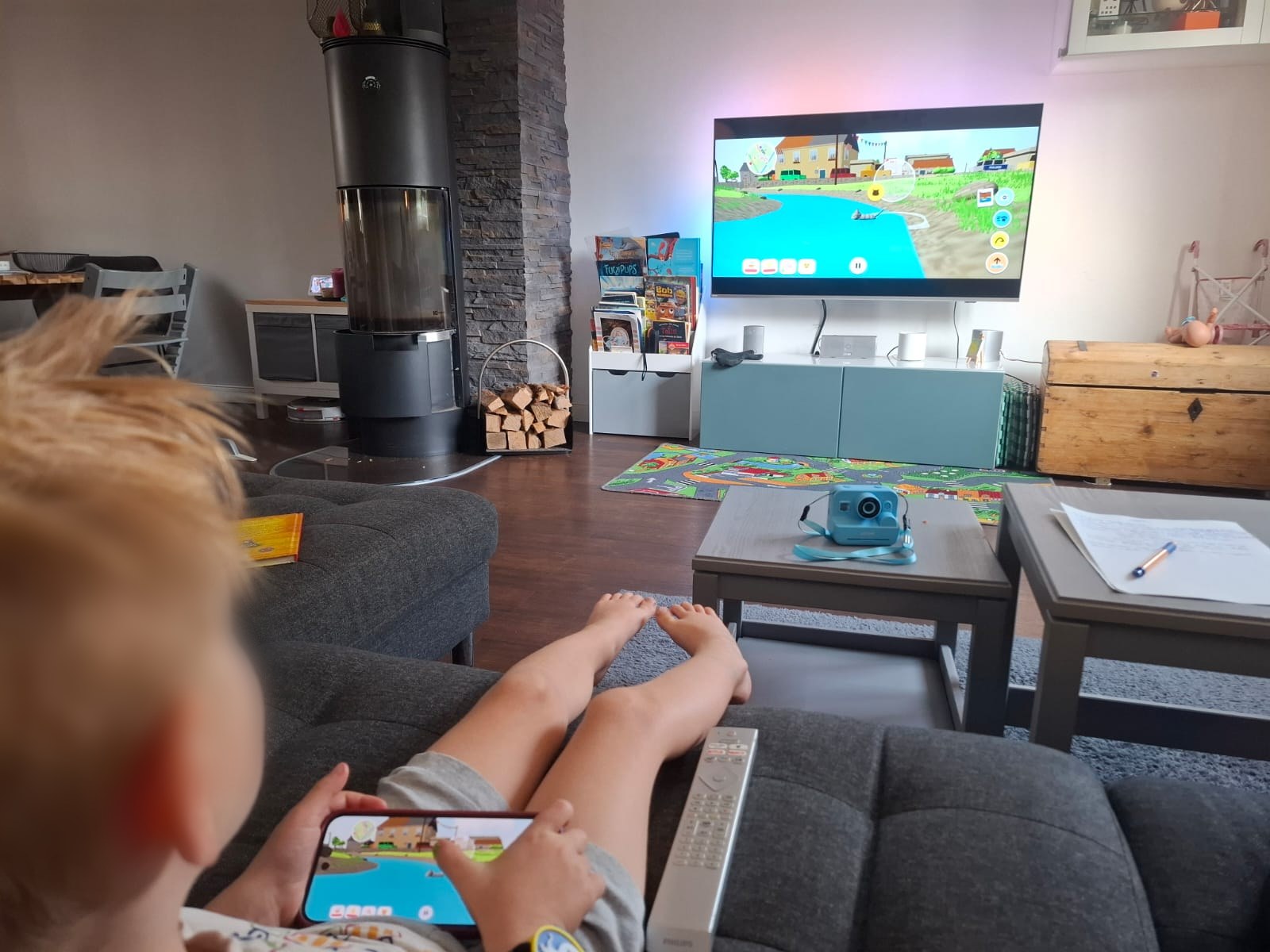 Mein Sohn auf dem Sofa, das Handy quer als Controller, auf dem Fernseher läuft Miez