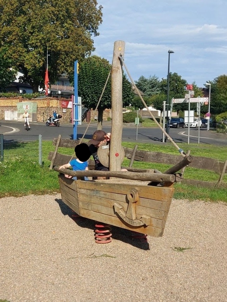 Das Spielplatz-Schiff aus Holz auf einer Feder, mit Mast, Tauen und eingeschnitztem Anker am Bug